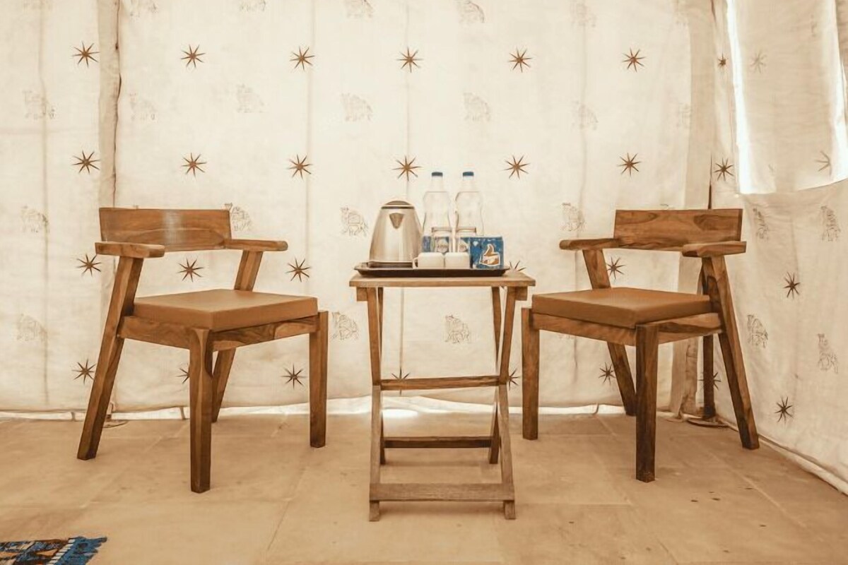Two wooden chairs and a small table with a tray of items in a room with patterned curtains.