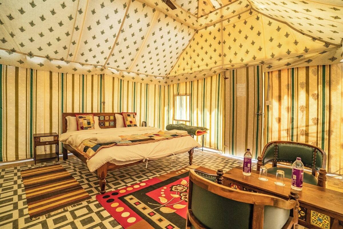A tent-style room with a bed, a wooden table with chairs, and a patterned rug.