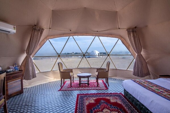 Una habitación tipo tienda de campaña con una cama, dos sillas, una mesita y vistas a un paisaje lejano.