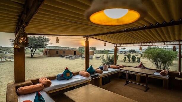 An outdoor seating area with wooden benches and tables, a covered roof, and a view of the surrounding landscape. - Tokyo Desert Camp (Jaisalmer)