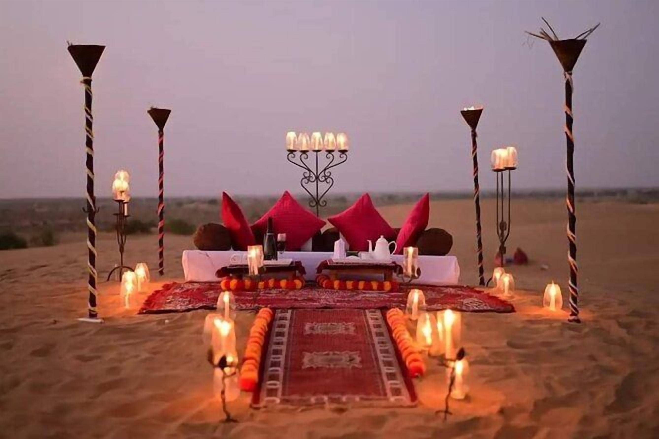 Paisaje desértico con una cama, almohadas y velas dispuestas para una noche romántica.