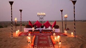 Paisaje desértico con una cama, almohadas y velas dispuestas para una noche romántica.