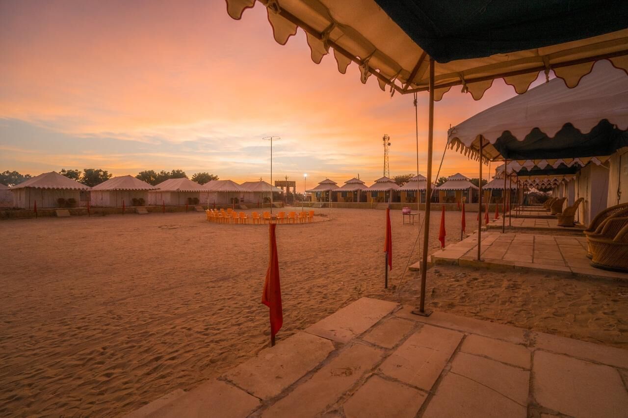 A desert camp with yurts, arranged in rows, and a paved walkway leading to a covered area.