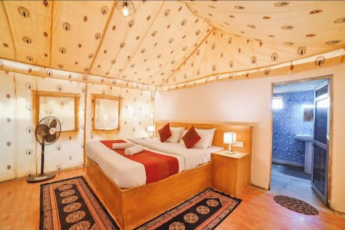 A bedroom with a wooden bed, a nightstand, a floor fan, and a patterned rug.