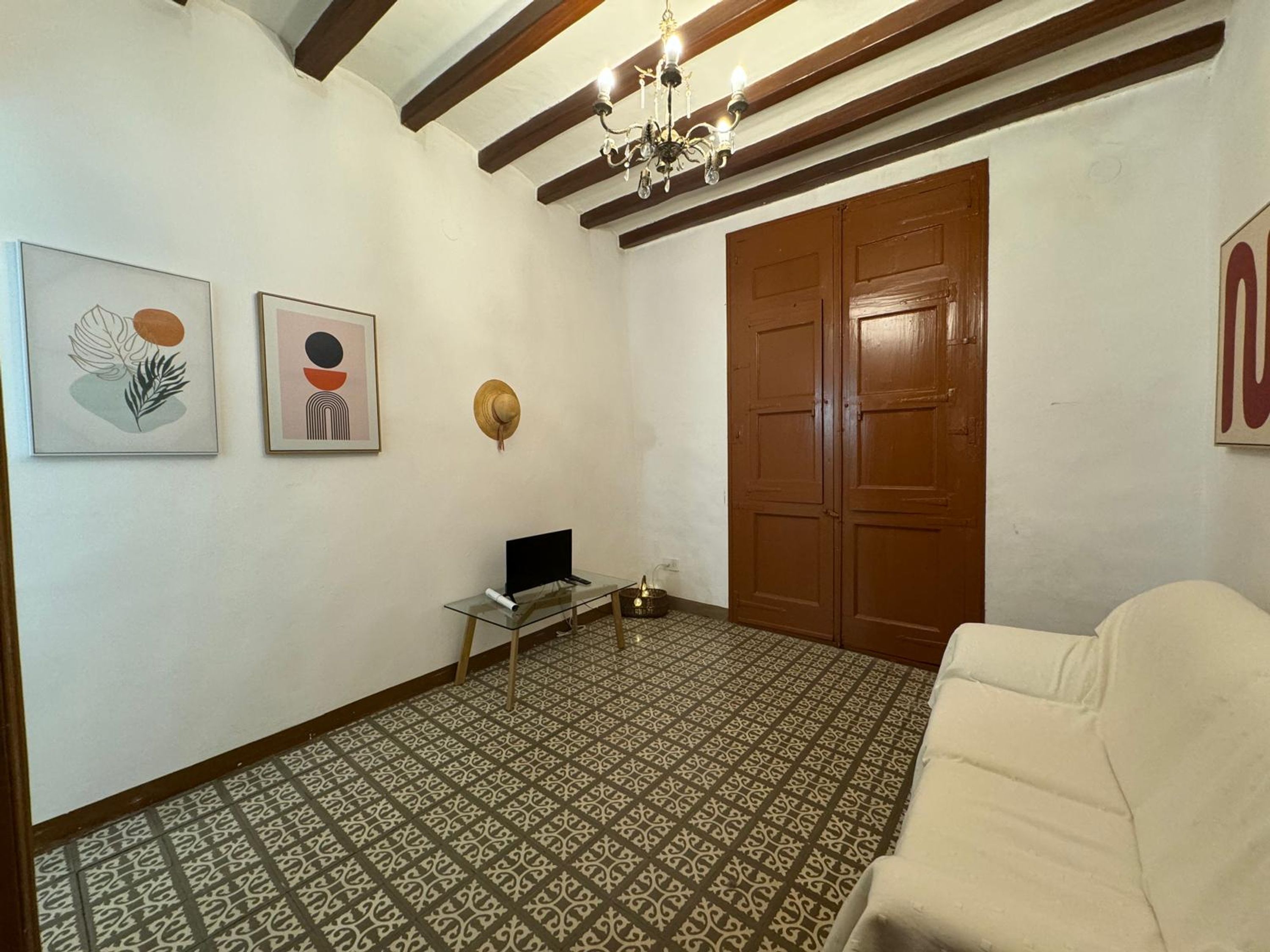 A room with patterned flooring, a white sofa, a desk with a computer, and two doors.