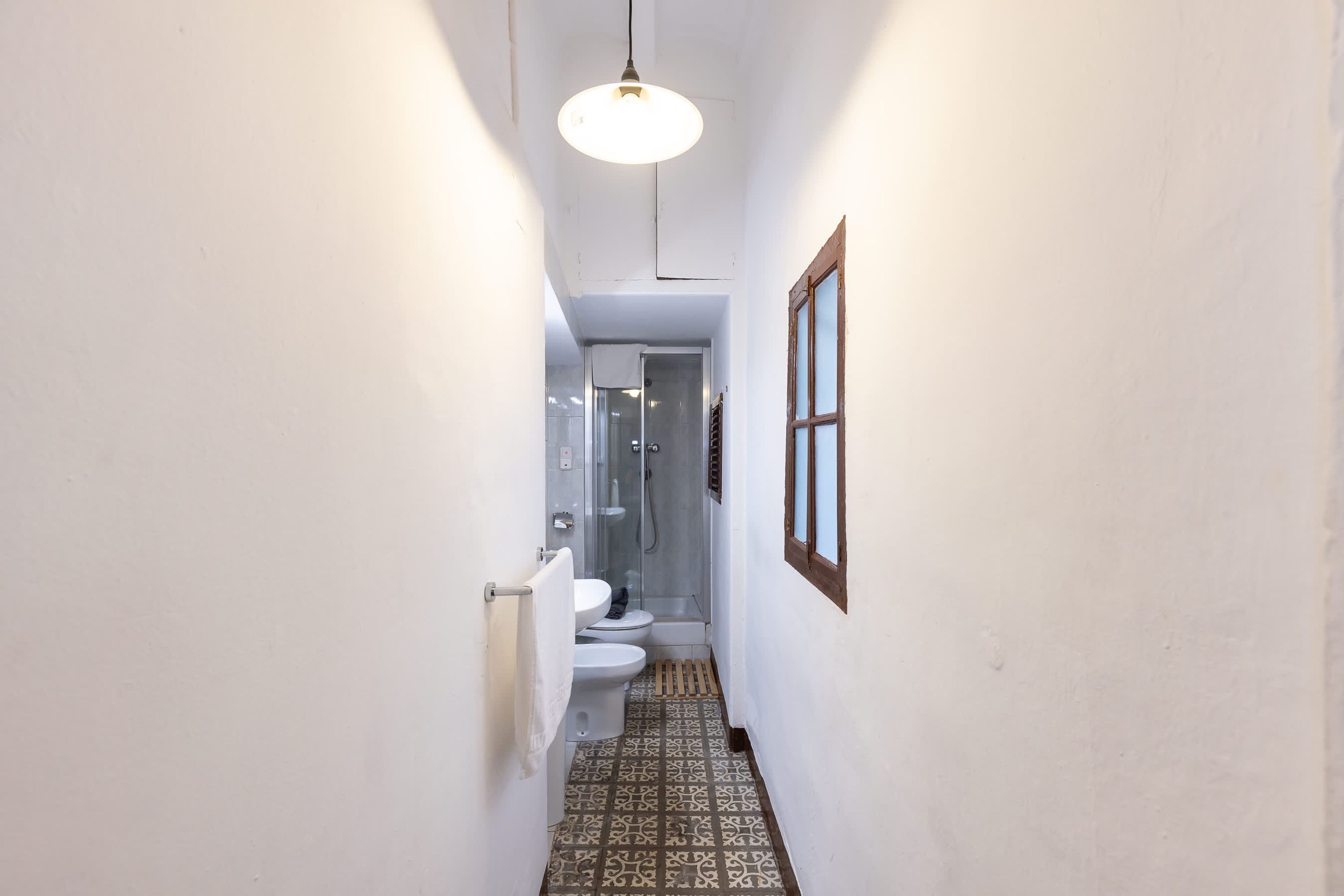 Um corredor estreito com piso estampado, um toalete e área de chuveiro.