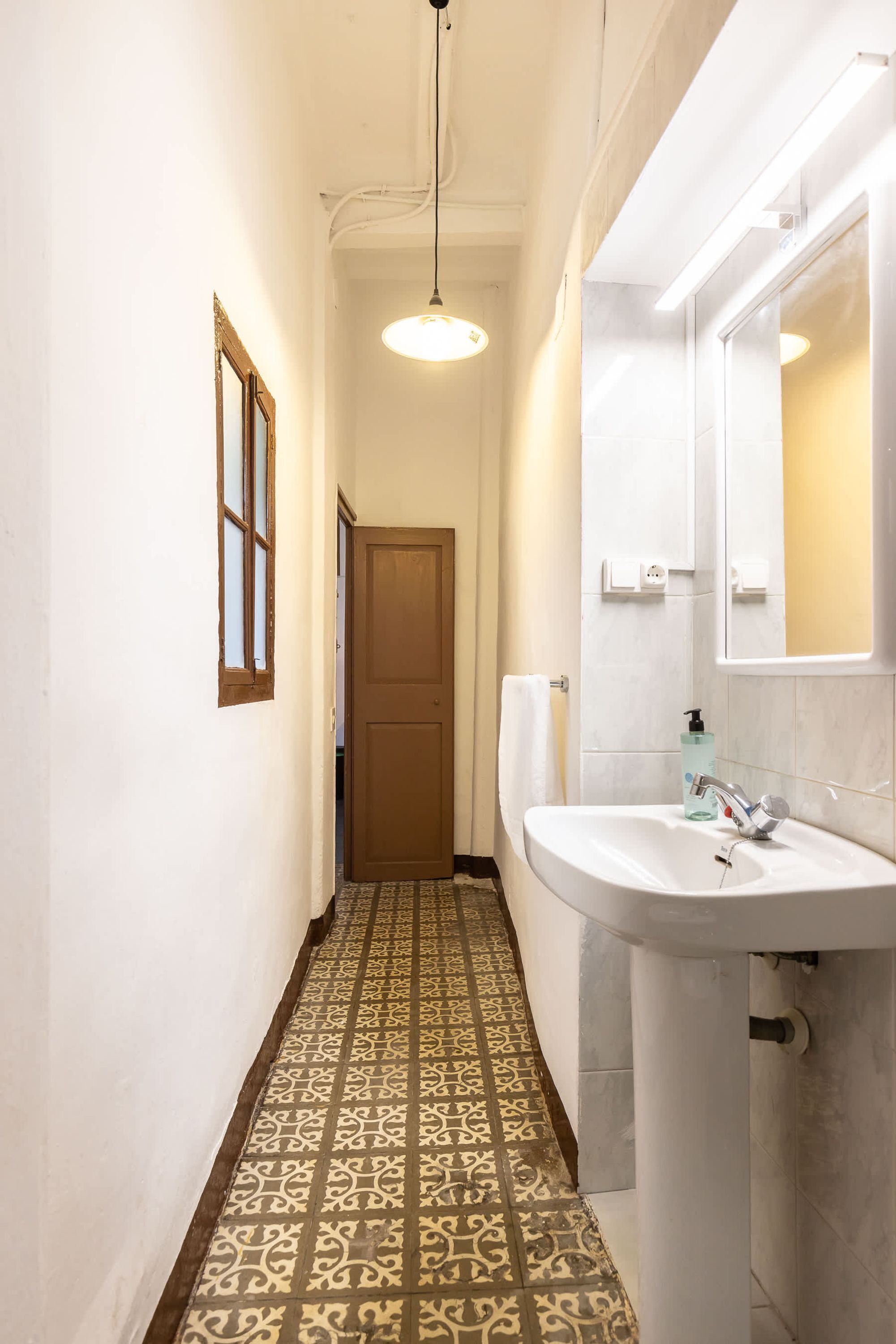 A narrow hallway with patterned floor tiles, a white sink with a mirror, and a door at the end.