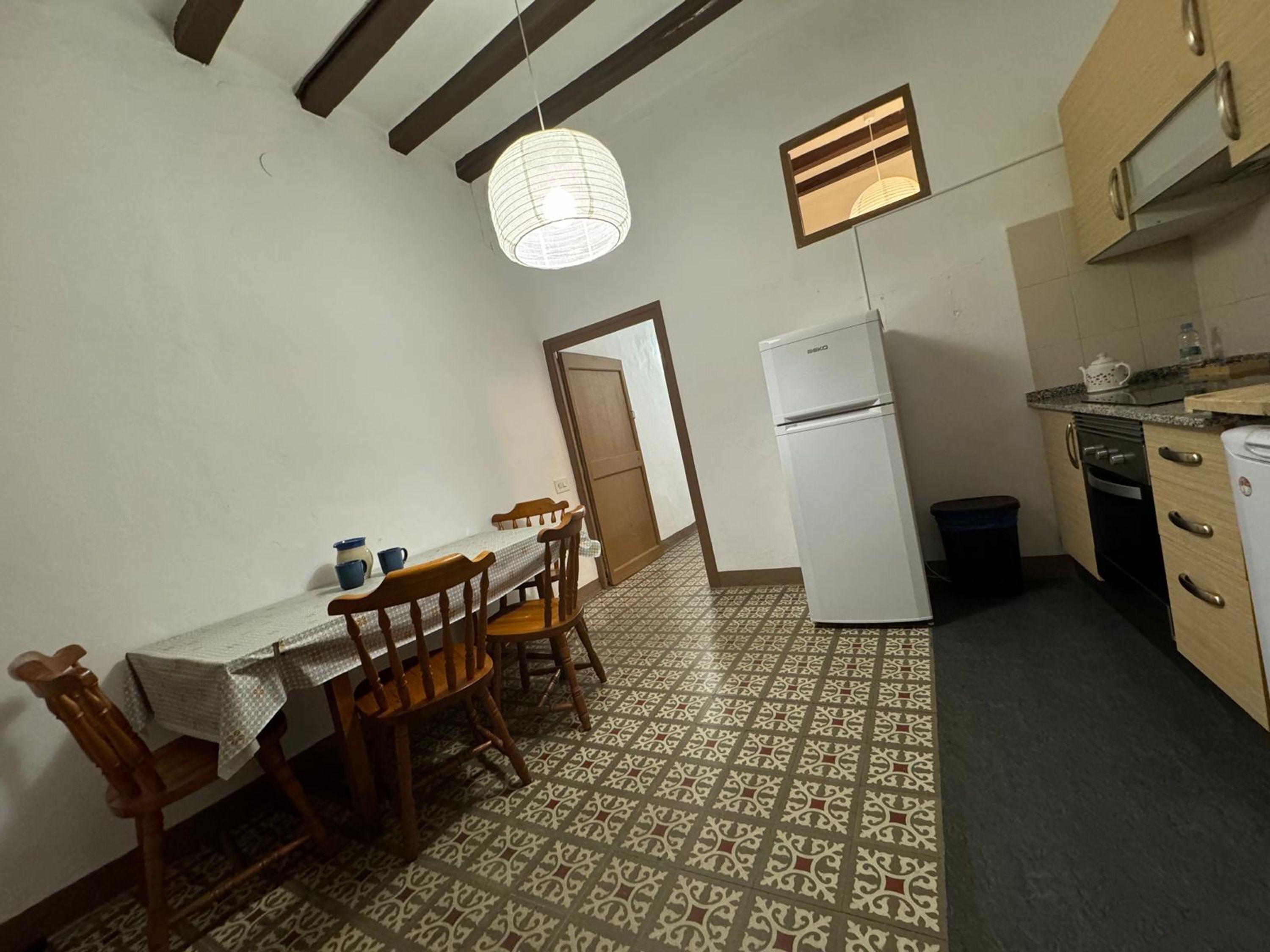 A compact kitchen with a dining table, chairs, a refrigerator, and a patterned floor.
