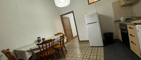 A compact kitchen with a dining table, chairs, a refrigerator, and a patterned floor.