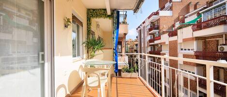 A balcony with a glass door, a small table with chairs, and potted plants.
