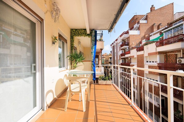 A balcony with a glass door, a small table with chairs, and potted plants.
