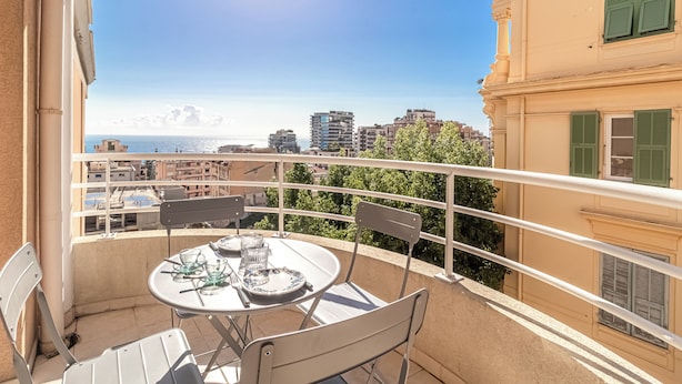 Een balkon met een tafel voor twee personen, met uitzicht op een stadsgezicht met gebouwen en een heldere lucht.