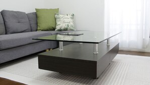 A modern living room with a glass-top coffee table, grey sofa, and a green pillow. - NEW OPEN 2 minutes walk from Higashi-Shinjuku Station (新宿区)
