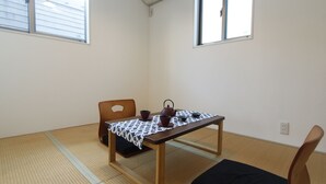 A room with tatami flooring, a low table with a patterned tablecloth, a tea set, and a chair. - NEW OPEN 2 minutes walk from Higashi-Shinjuku Station (新宿区)