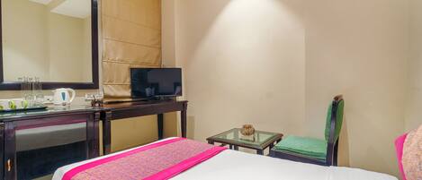 Habitación de hotel con cama, escritorio con televisor, espejo, mesita de noche con lámpara y una silla.