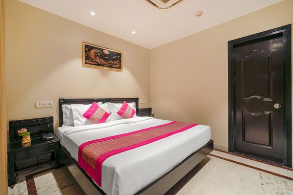 Een net opgemaakt bed met wit en roze beddengoed, een donker houten hoofdbord en een decoratief schilderij erboven.