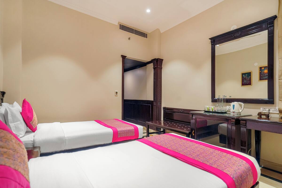 Een hotelkamer met twee bedden, een grote spiegel, een bureau met een waterkoker en een raam.