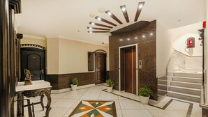 A hotel lobby with a marble floor, a decorative tile pattern, a reception desk, two potted plants, and a staircase with a fire extinguisher. - One Earth City Heart Amritsar (Amritsar)