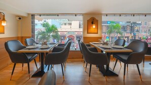 A restaurant with modern black chairs and tables, large windows offering a view of the street and buildings outside. - One Earth City Heart Amritsar (Amritsar)
