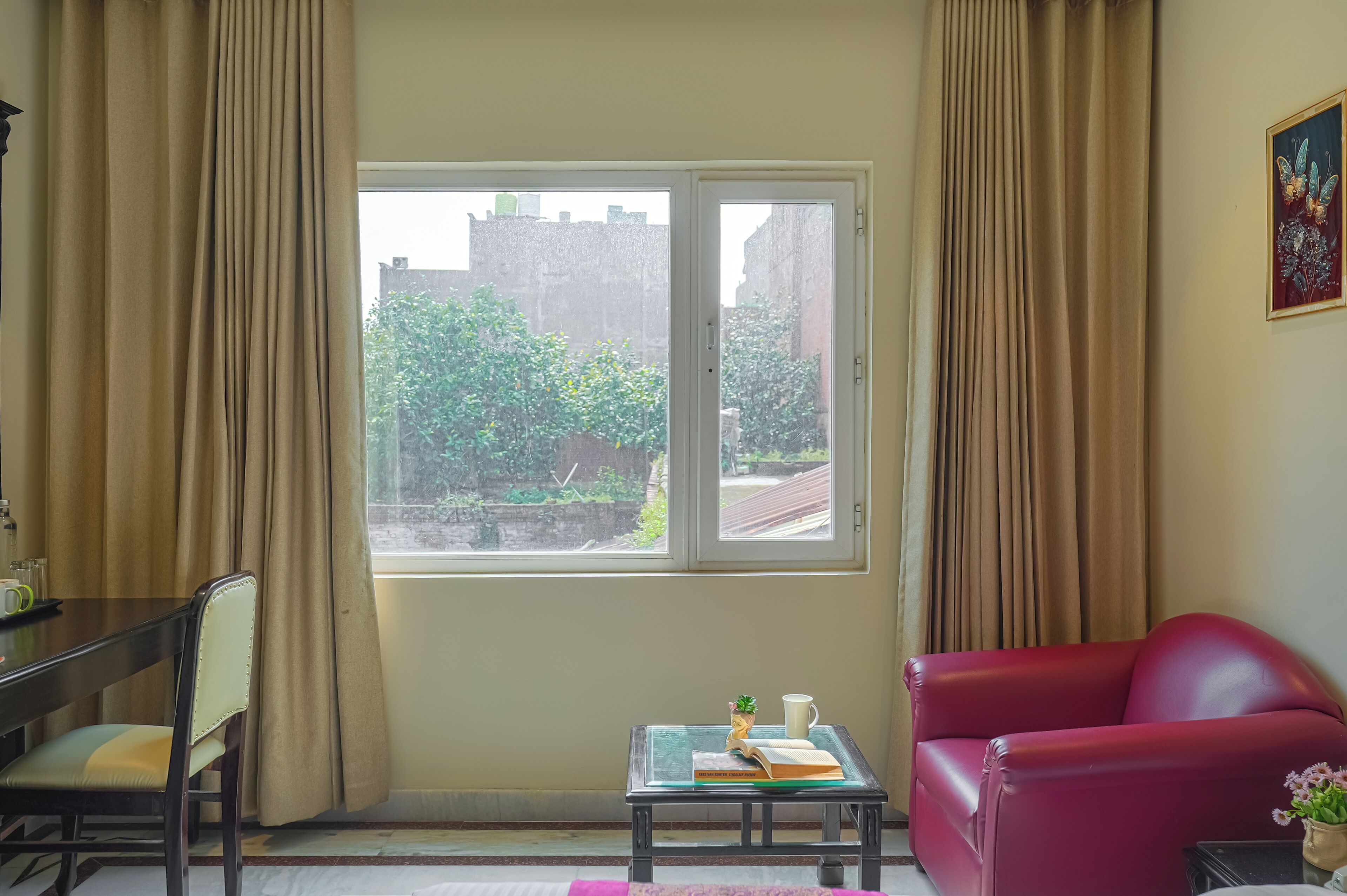 Ein Zimmer mit Fenster, einem roten Sofa, einem Glastisch mit Buch und Tasse sowie einem Sessel.