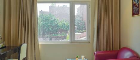 Ein Zimmer mit Fenster, einem roten Sofa, einem Glastisch mit Buch und Tasse sowie einem Sessel.