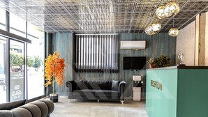 A reception area with a modern design, featuring a sofa, a reception desk, and a decorative plant. - ARİA SUİT KONAKLAMA (Mezitli)