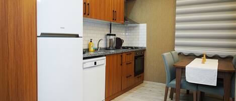 Cocina compacta con armarios de madera, un refrigerador blanco, una estufa y una mesa de comedor con sillas.