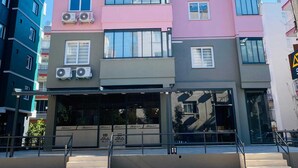 A multi-story building with air conditioning units on the exterior, a visible entrance with a glass door, and a sign indicating 'ARIA SUIT'. - ARİA SUİT KONAKLAMA (Mezitli)