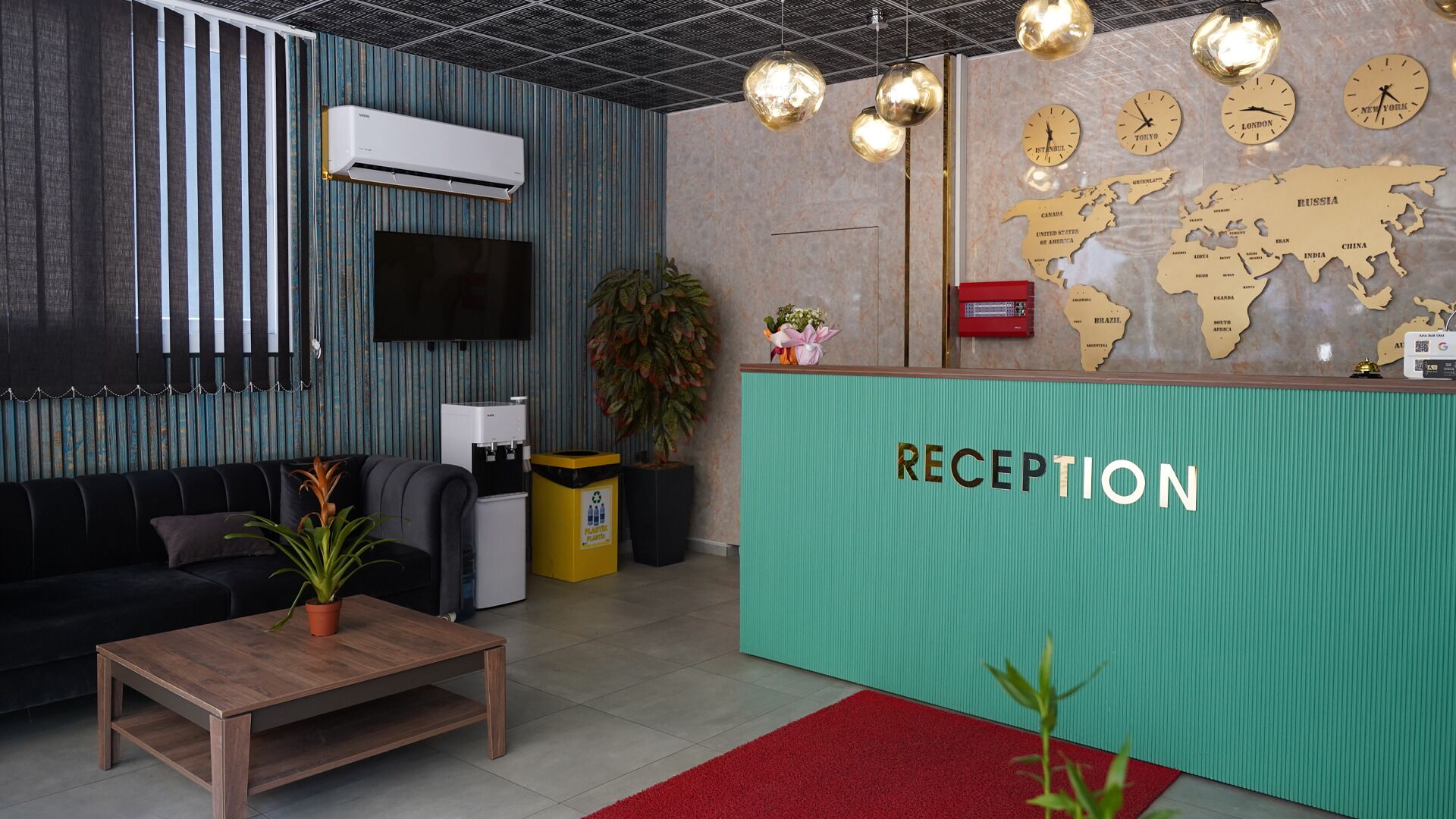 Un espace d’accueil avec un comptoir vert, un canapé noir, une table basse en bois, une plante en pot et une carte du monde avec des horloges.