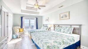 Een slaapkamer met twee bedden, een plafondventilator, een raam met gordijnen en een stoel.