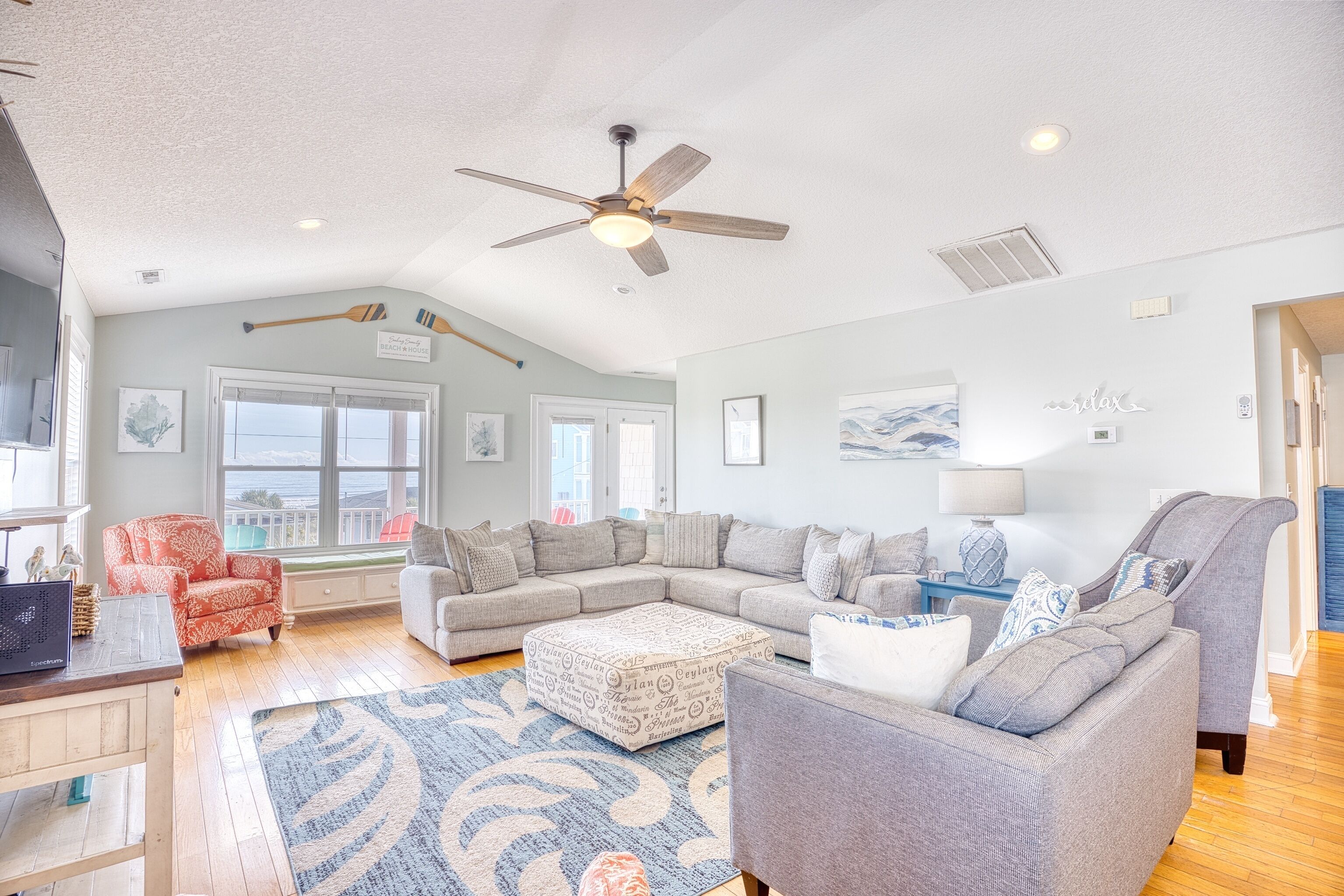 A spacious living room with a large sectional sofa, a grey armchair, and a ceiling fan.
