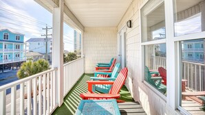 Een balkon met een rij kleurrijke Adirondack-stoelen, een kleine tafel en uitzicht op de straat en gebouwen.