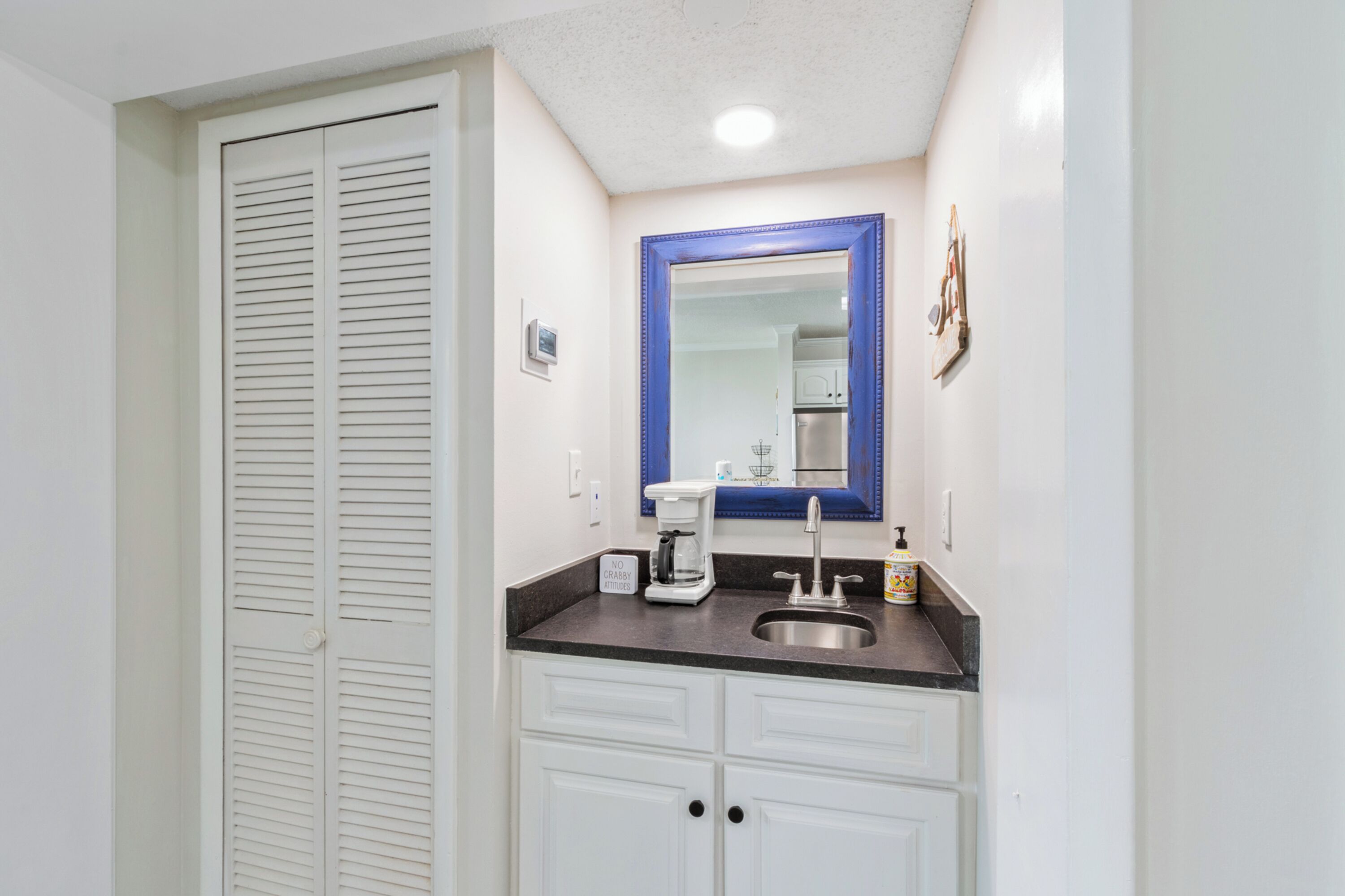 Une salle de bain avec une porte blanche, un lavabo avec un miroir et une machine à café.