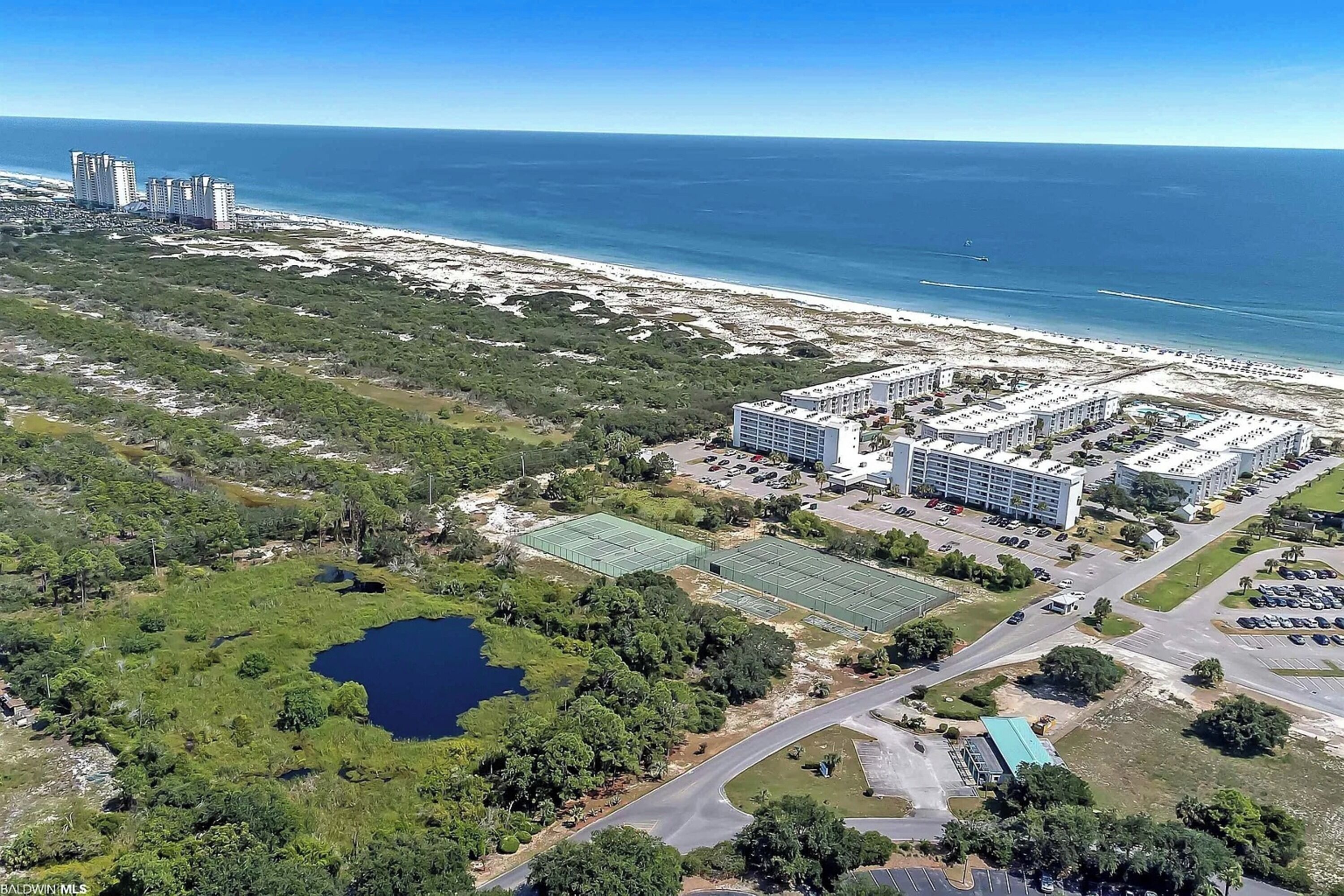 Vue aérienne d’un hôtel situé sur la côte, composé de plusieurs bâtiments, avec une plage et un lac.