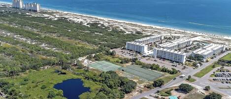 Vue aérienne d’un hôtel situé sur la côte, composé de plusieurs bâtiments, avec une plage et un lac.