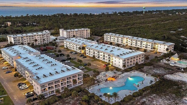 Een resort met meerdere gebouwen, een zwembad en uitzicht op de oceaan bij zonsondergang.