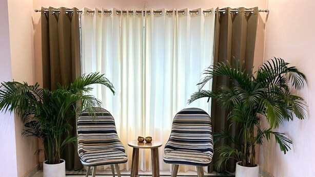 A seating area with two striped chairs, a small round table, and two potted plants. - Solhouse Serviced Apartments Gurgaon (Gurugram)