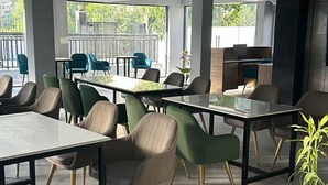 A spacious indoor dining area with multiple tables and chairs, large windows, and a potted plant. - Solhouse Serviced Apartments Gurgaon (Gurugram)