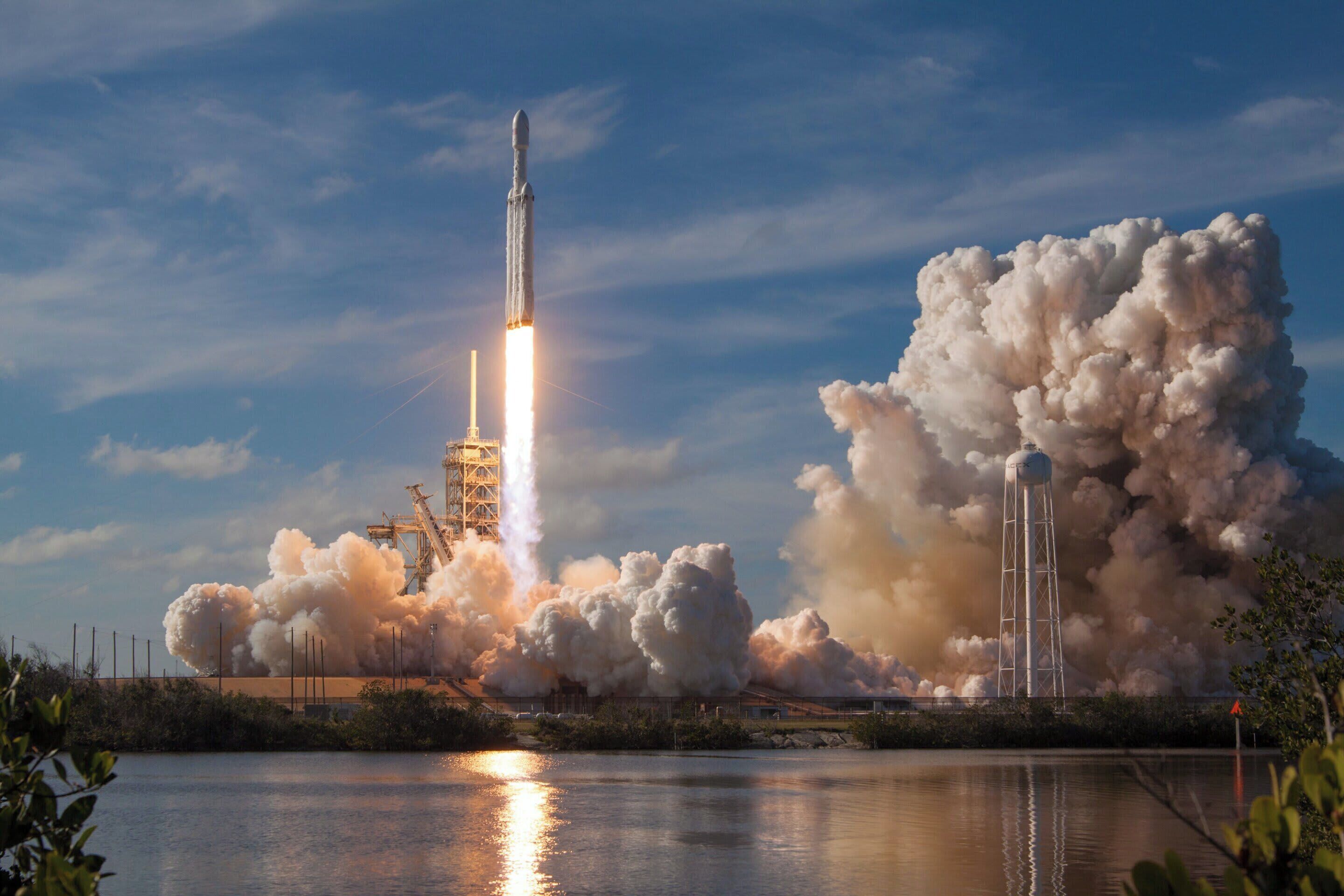 A rocket launch with a large plume of smoke and a water tower in the background.