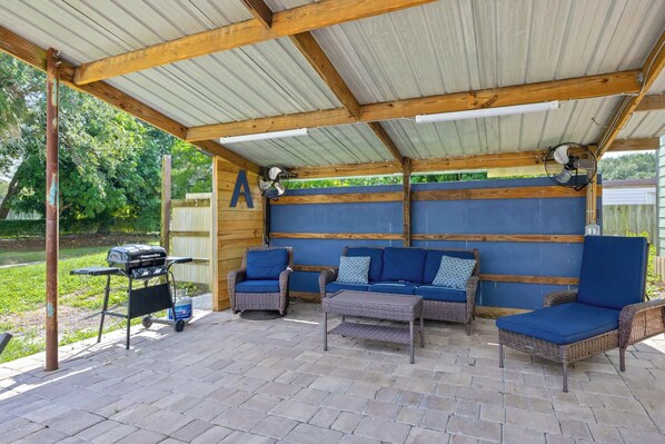 Une terrasse couverte avec un barbecue, des meubles en osier et un mur bleu.