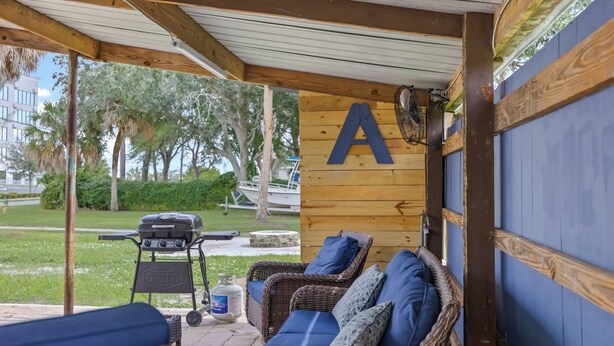 Eine überdachte Terrasse mit Grill, Korbmöbeln und einem großen 'A' an der Wand.
