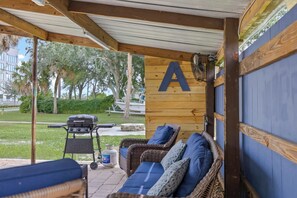 Eine überdachte Terrasse mit Grill, Korbmöbeln und einem großen 'A' an der Wand.