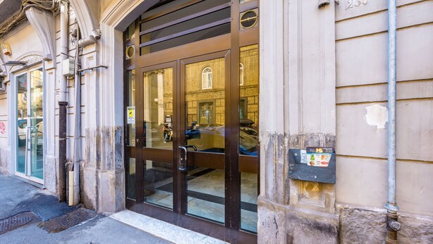 L’entrée d’un immeuble, avec une porte en verre, une boîte aux lettres et le numéro 235 inscrit sur le mur.