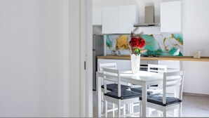 Une cuisine moderne avec des meubles blancs, un plan de travail en bois et un coin repas comprenant des chaises blanches et un vase de fleurs.