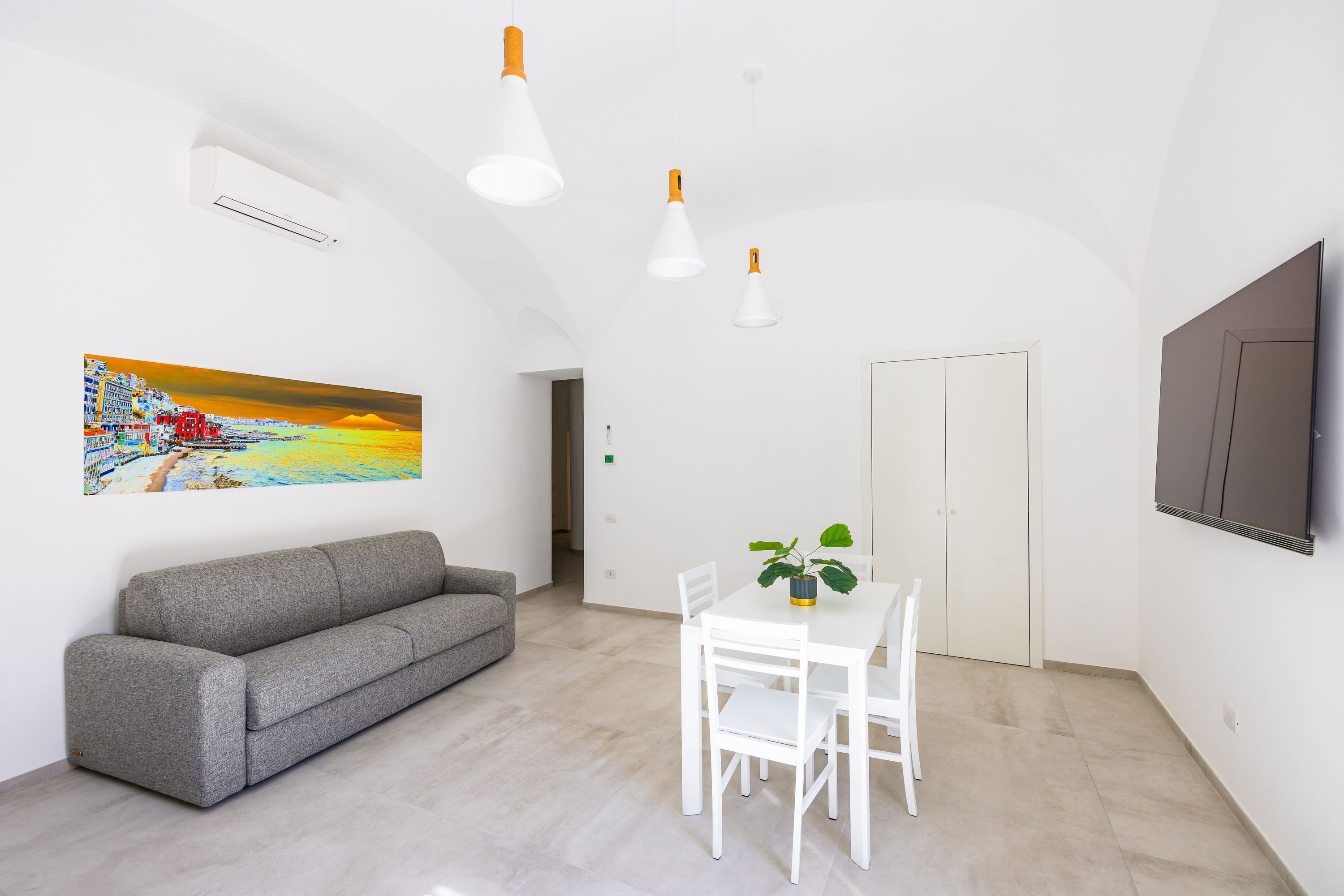 Une pièce moderne avec un canapé gris, une table à manger blanche avec des chaises et un tableau au mur.