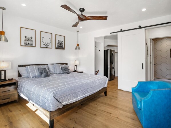 A modern bedroom with a wooden bed, a ceiling fan, and framed artwork on the wall.