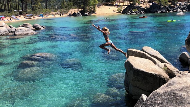 A clear view of a natural pool with rocky edges, surrounded by a forested area and a sandy beach.