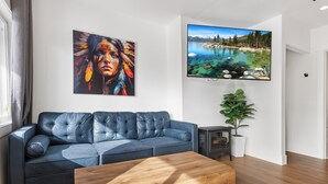 A modern living room with a blue leather sofa, a wooden coffee table, a flat-screen TV, and a painting of a landscape.