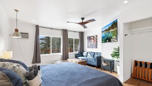 A modern bedroom with a large bed, a sofa, a ceiling fan, and a window with curtains.