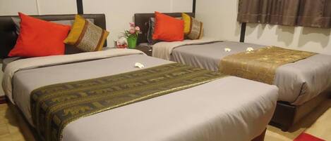 A hotel room with two beds, each with a patterned bedspread and multiple pillows. There is a small table with a vase of flowers and a red rug on the floor.